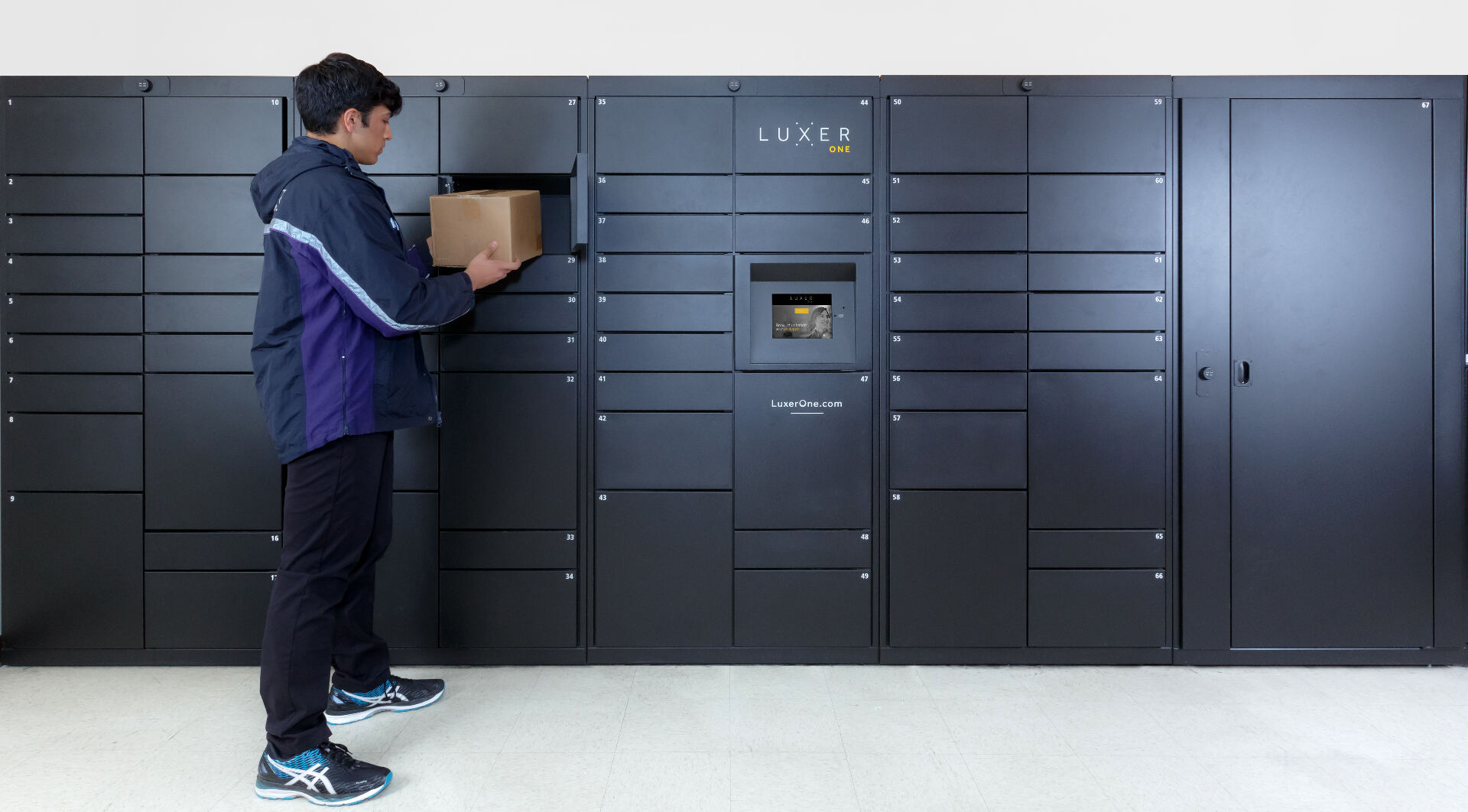 Luxer One indoor electronic package lockers installed in an apartment mailroom — delivery carrier dropping off a resident's package into a smart parcel locker